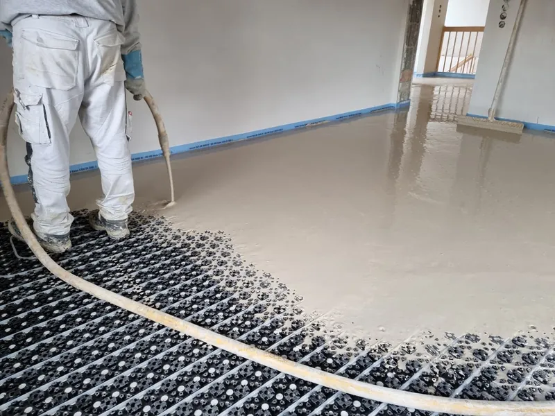 Mitarbeiter der Topal GmbH glättet Fließestrich über den Heizrohren einer Fußbodenheizung